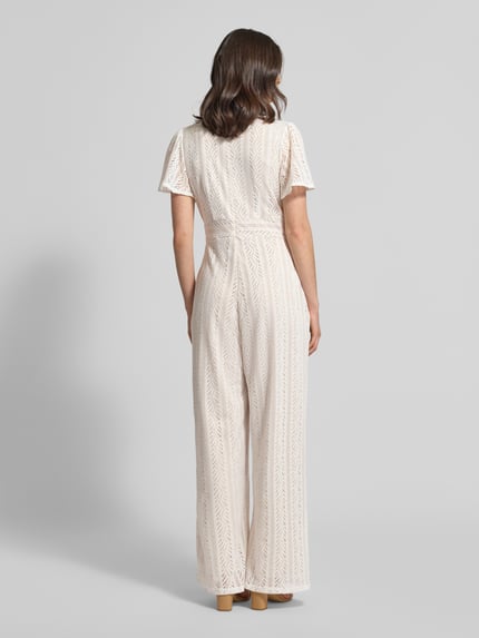Frauenmodel trägt Jumpsuit mit Lochstickerei und rückseitigem Reißverschluss von Apricot in Creme, Ganzkörperansicht Rückansicht, Regular Fit, V-Ausschnitt, Rückenlänge 38 cm, Brustweite 43 cm, Ärmellänge 22 cm, Gesamtlänge 148 cm, Innenbeinlänge 75 cm, leichte Struktur mit feinen Durchbrüchen.
