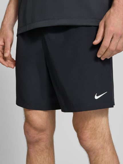 Männermodel trägt schwarze Shorts mit Logo-Print und Eingrifftaschen von NIKE TRAINING, glatte Textur, Nahaufnahme Oberschenkel.
