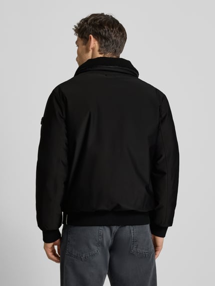 Männermodel trägt Bomberjacke mit Stehkragen Modell 'Ginster' von khujo in Schwarz, Material-Mix, gerippte Abschlüsse, Ganzkörperansicht Rückansicht.