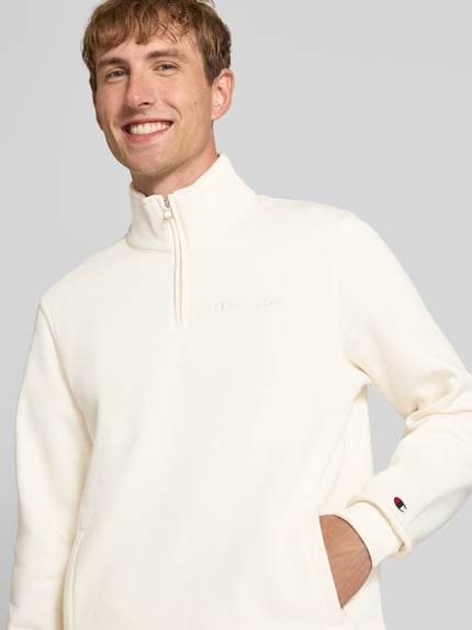 Männermodel trägt Sweatshirt mit Label-Details von Champion, mieszanka bawełny, prosty krój, kołnierz zapinany, wpuszczane kieszenie, długość tyłu w rozmiarze M: 72 cm, długość rękawów w rozmiarze M: 71 cm, jasny kolor, gładka faktura, nahaufnahme górnej części ciała.