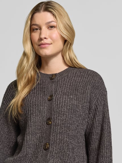 Kobiece model prezentuje kardigan rozpinany Loose Fit Strickjacke mit einreihiger Knopfleiste model 'LEA' od VERO MODA w szarym kolorze, wyraźna tekstura dzianiny, duże guziki, zbliżenie na górną część ciała