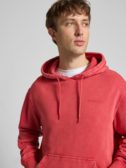 Männermodel trägt Hoodie mit Label-Stitching und Känguru-Tasche von Dickies in Rot, Relaxed Fit, Baumwoll-Mix, Nahaufnahme Oberkörper.