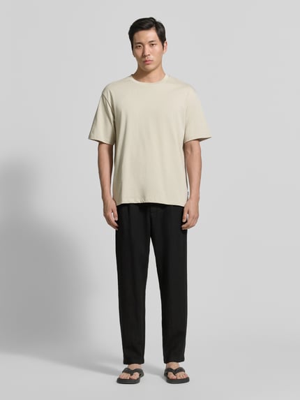 Männermodel trägt Tapered Fit Leinenhose mit Eingrifftaschen von MCNEAL, schwarze Stoffhose aus Leinen, Ganzkörperansicht von vorne. Bundweite bei Größe M: 45 cm, Innenbeinlänge bei Größe M: 76 cm, Paspeltaschen am Gesäß.