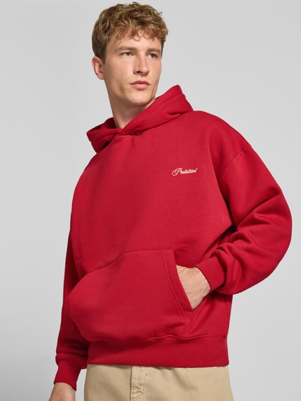 Männermodel trägt Relaxed Fit Hoodie aus Baumwoll-Mix mit Label-Stitching von PROHIBITED in Rot, Känguru-Tasche, Ganzkörperansicht von vorne.
