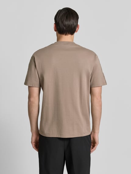 Męski model nosi Relaxed Fit T-Shirt aus reiner Baumwolle Modell 'DROSTEE' von HUGO w jednolitym, beżowym kolorze, krój relaxed fit, krótki rękaw, okrągły dekolt, z naszywką z logo, jersey z czystej bawełny, widok całej sylwetki od tyłu.