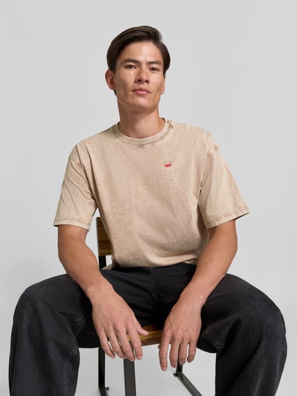 Männermodel trägt T-Shirt mit Label-Detail von Diesel in Beige, reine Baumwolle, gerader Schnitt, Nahaufnahme Oberkörper, KI-modifiziertes Bild.