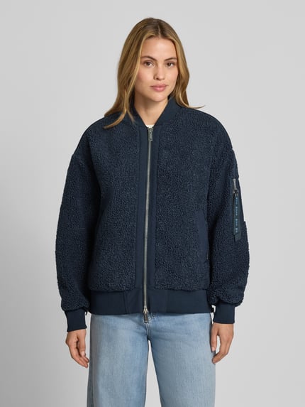 Frauenmodel trägt Teddyjacke mit Stehkragen Modell 'Emeline' von MOS MOSH in Dunkelblau, lockere Passform, Reißverschlusstasche am Ärmel, Zweiwege-Reißverschluss, seitliche Eingrifftaschen, elastische Abschlüsse, dezentes Label-Detail, strukturierte Oberfläche, Ganzkörperansicht von vorne.