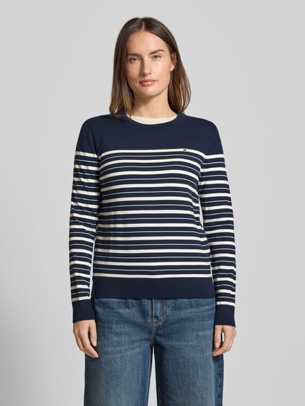 Kobiece model nosi Regular Fit Strickpullover aus Baumwoll-Mix od Tommy Hilfiger, bawełniany sweter w paski, niebiesko-białe kolory, wzór pasków, ściągacze na rękawach i dole, crew neck, logo, cała sylwetka z przodu.
