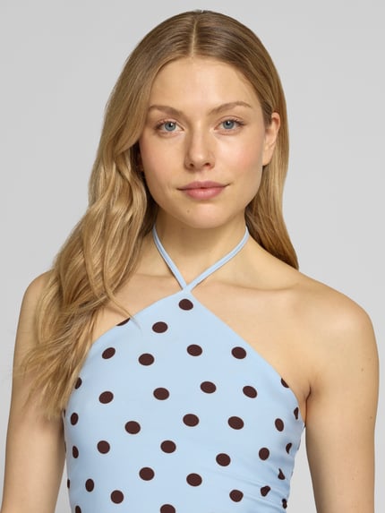 Frauenmodel trägt Neckholder-Top im Allover-Look Modell 'Bowie' von Forever New, hellblau mit braunen Punkten, Material-Mix mit Stretch-Anteil, Körpernahe Passform, Nahaufnahme Oberkörper.