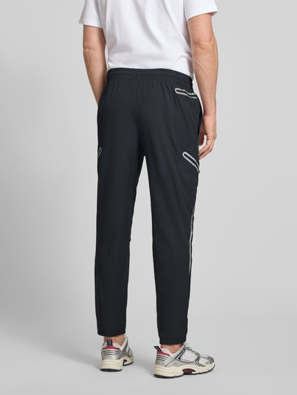 Männermodel trägt Regular Fit Sweatpants mit Logo-Print Modell 'Unstoppable' von Under Armour in Schwarz, Elastischer-Material-Mix, Cargo-Taschen mit Reißverschluss, Elastischer Bund, Innenbeinlänge bei Größe M 79 cm, Ganzkörperansicht Rückansicht.