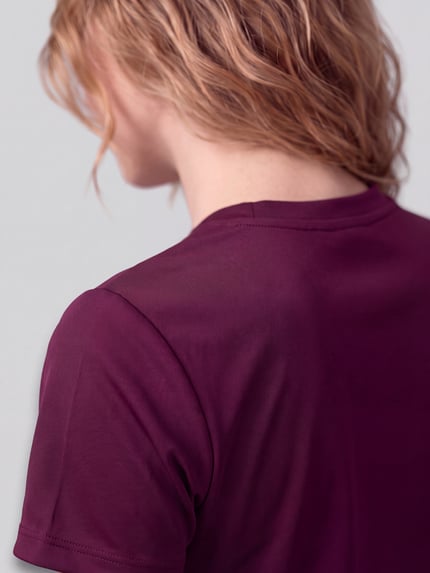 Frauenmodel trägt T-Shirt mit Label-Stitching und Rundhalsausschnitt von PUMA aus reiner Baumwolle in Dunkelviolett, Nahaufnahme Rückansicht.