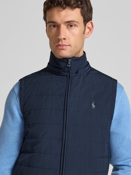 Mężczyzna model nosi Kamizelka pikowana z kapturem i wyhaftowanym logo od Polo Ralph Lauren, krój regular fit, stójka, zamek błyskawiczny, kolor granatowy, szerokość ramion 42 cm, szerokość klatki piersiowej 58 cm, długość tyłu 31 cm, detaliczny materiał, nahaufnahme górnej części ciała.