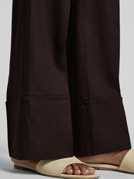Frauenmodel trägt Hose aus Leinen-Viskose-Mix Modell 'Ottavie' von mbyM, dunkler Farbton, sichtbare Bügelfalten, Nahaufnahme Beinbereich. Damen Hose aus Leinen-Viskose-Mix, Wide Leg, Bügelfalten, Bundweite bei Größe S: 39 cm, Innenbeinlänge bei Größe S: 81 cm.