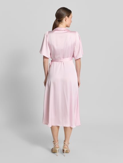 Modelka nosi różowe satynowe Midikleid in Wickel-Optik Modell 'VIENNA RAVENNA' od Vila, krój taliowany, długość do łydek, widok całej sylwetki z tyłu. Szerokość w rozmiarze 36: 50 cm, długość pleców: 125 cm, długość rękawa: 30 cm.