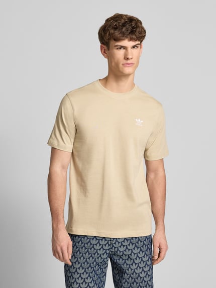 Männermodel trägt T-Shirt mit Label-Stitching von adidas Originals in Beige, reine Baumwolle, Regular Fit, Nahaufnahme Oberkörper.