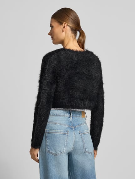 Kobiece model prezentuje Regular Fit Bolero mit Zierschleife od Apricot w czarnej imitacji dzianiny, krótki krój, długość tyłu w rozmiarze S: 39 cm, długość rękawów: 64 cm, widok całej sylwetki z tyłu.
