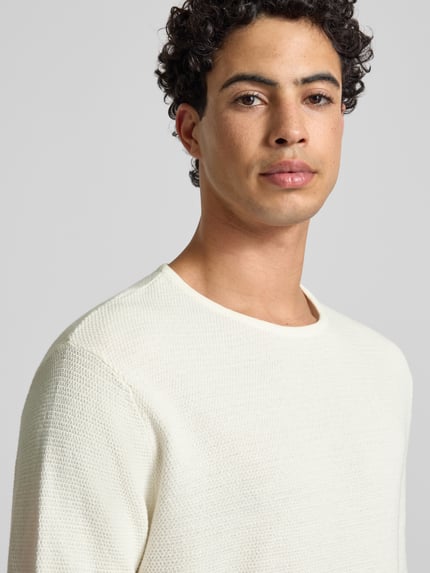 Männermodel trägt Strickpullover mit geripptem Rundhalsausschnitt Modell 'GEORGE' von Jack & Jones, cremefarben, Nahaufnahme Oberkörper. Baumwoll-Mix, lockerer Schnitt.