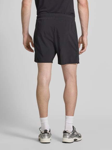 Männermodel trägt schwarze Regular Fit Shorts mit integriertem Slip Modell 'ICON' von ASICS TIGER, elastischer Bund, Rückansicht Ganzkörperansicht.