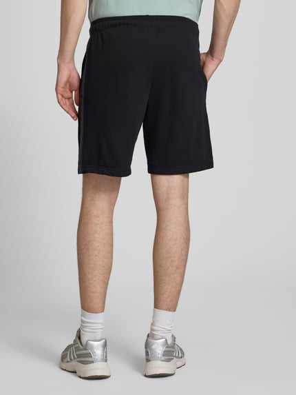 Männermodel trägt schwarze Shorts mit Logo und elastischem Bund von CHAMPION aus Baumwoll-Mix, Regular Fit, Rückansicht Ganzkörperansicht.