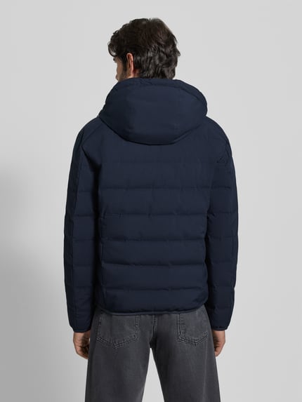 Męskimodel nosi Regular Fit Daunenjacke mit Kapuze von Marc O'Polo, jednolity kolor, długi rękaw, wypełnienie z puchu i pierza, wodoszczelny, wiatroszczelny, oddychający materiał, elastyczne wykończenia, wpuszczane kieszenie, kieszeń wewnętrzna, zamek błyskawiczny dwustronny, odpinany kaptur z tunelem. Ganzkörperansicht Rückansicht.