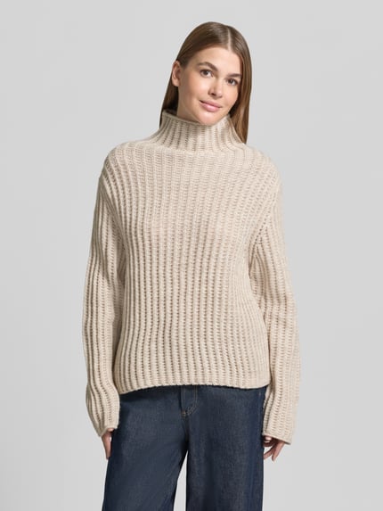 Frauenmodel trägt Strickpullover mit Stehkragen Modell 'ARWIE' von DRYKORN, beige, grob gestrickt, Alpaka-Mix, Regular Fit, Ganzkörperansicht von vorne.