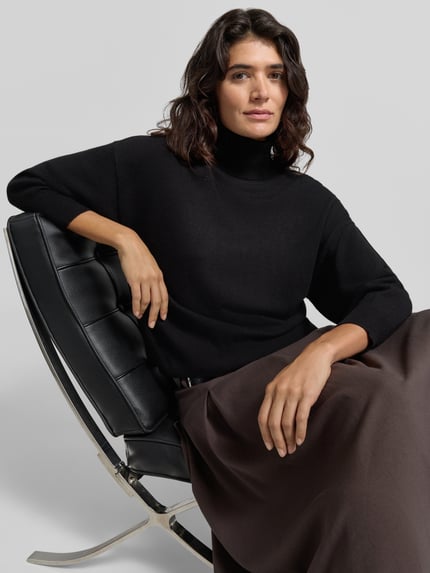Frauenmodel trägt Relaxed Fit Strickpullover aus reiner Wolle von Max Mara in Schwarz, Rollkragen, 3/4-Arm, weiche Textur, Nahaufnahme Oberkörper.