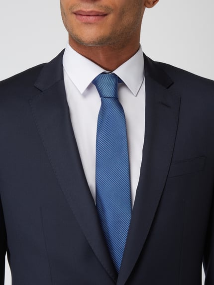 Männermodel trägt Krawatte aus reiner Seide von Monti in Blau, klassische Passform, feine Textur, Label-Detail sichtbar, Nahaufnahme Oberkörper.