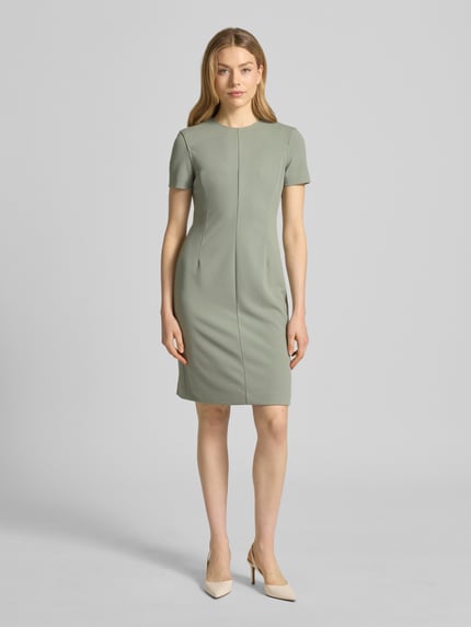 Frauenmodel trägt knielanges Etuikleid mit Rundhalsausschnitt von Calvin Klein Womenswear, Material-Mix, sanftes Grün, Ganzkörperansicht von vorne.