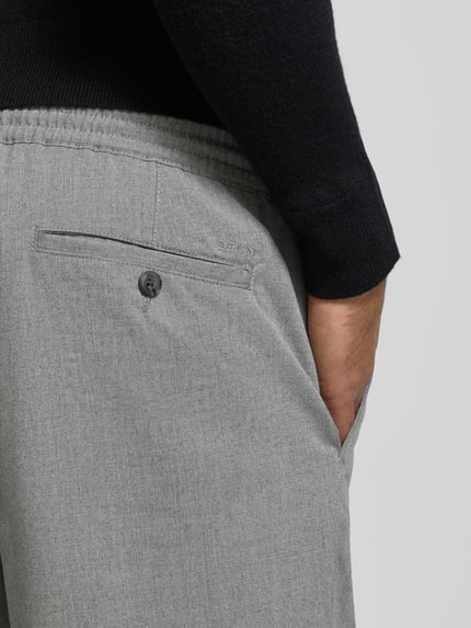 Männermodel trägt spodnie materiałowe z elastycznym pasem, tunel, wpuszczane kieszenie, kieszeń z tyłu, MCNEAL, szara faktura, detailaufnahme.