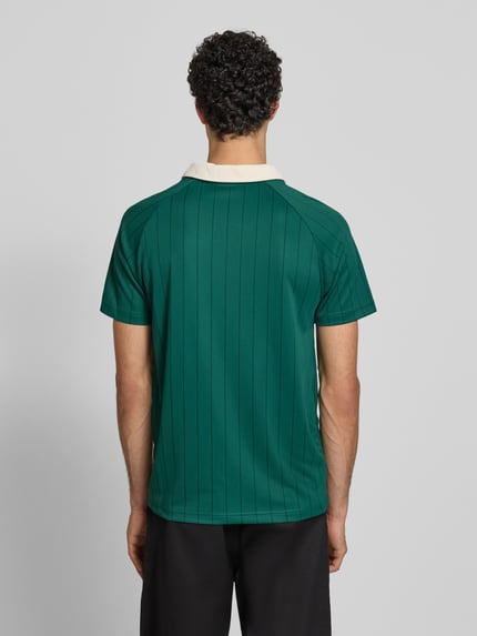 Męski model nosi Regular Fit T-Shirt mit Umlegekragen von KARL KANI w zielonym kolorze z wyhaftowanym logo, długość tyłu 67 cm, krótki rękaw, krój regular fit, widok na całe ciało z tyłu.