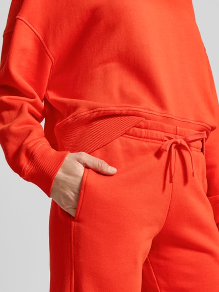 Frauenmodel trägt Sweatpants aus Baumwoll-Modal-Mix von Juvia in leuchtendem Orange mit elastischem Bund und Tunnelzug, Nahaufnahme Oberkörper.