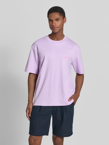 Männermodel trägt Oversized T-Shirt mit Label-Print von Lindbergh in Flieder, Reine Baumwolle, Rundhalsausschnitt, Ganzkörperansicht von vorne.