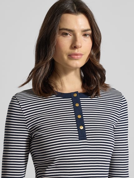 Frauenmodel trägt Slim Fit T-Shirt aus reiner Baumwolle von Tommy Hilfiger in Two-Tone-Optik, gestreift, Logo-Detail, Feinripp, Nahaufnahme Oberkörper.