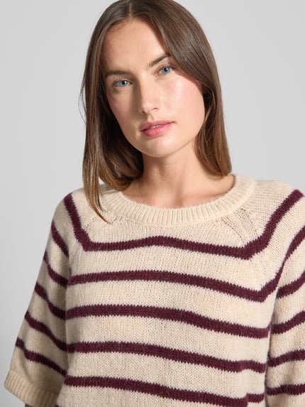 Frauenmodel trägt Strickpullover mit gerippten Abschlüssen von Milano Italy, cremefarben mit bordeauxfarbenen Streifen, Material-Mix mit Alpaka-Anteil, Rundhalsausschnitt, halblange Ärmel, lockerer Schnitt, Nahaufnahme Oberkörper.
