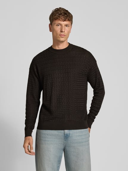 Männermodel trägt Strickpullover aus Viskose-Woll-Mix Modell 'VALDRIK' von DRYKORN in Schwarz mit feiner Struktur, Regular Fit, Ganzkörperansicht von vorne, Herrenmode.
