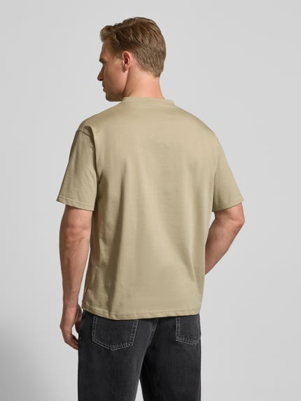 Männermodel trägt T-Shirt mit Motiv-Print Modell 'Baine' von WOODBIRD aus Bio-Baumwolle in Beige, Regular Fit, Ganzkörperansicht Rückansicht.