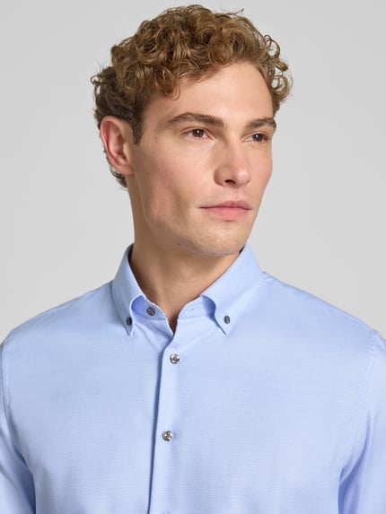 Männermodel trägt hellblaues Slim Fit Businesshemd aus reiner Baumwolle von Seidensticker, dezente Textur, Nahaufnahme Oberkörper.