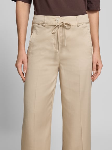 Vrouwenmodel draagt Wide Leg Pants met bindceintuur model 'Meeri bloom' van OPUS, lyocellmix met katoen, uitlopende fit, Franse steekzakken, vaste omslagzoom, fake achterzakken, beige kleur, knoop- en ritssluiting; close-up bovenlichaam vooraanzicht.