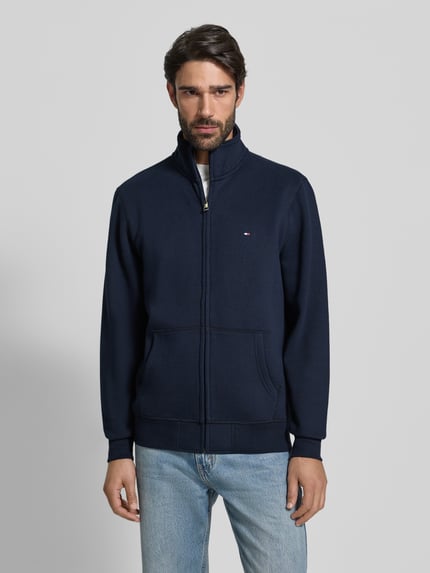 Männermodel trägt Regular Fit Sweatjacke aus Baumwoll-Mix von Tommy Hilfiger in Dunkelblau mit Stehkragen und Label Stitching, Ganzkörperansicht von vorne.