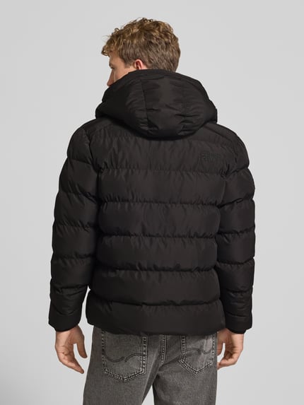 Männermodel trägt schwarze Steppjacke mit Label-Stitching und Kapuze von Superdry, strukturierte Oberfläche, Ganzkörperansicht Rückansicht. Herren Steppjacke, gerader Schnitt, Kapuze mit Kordelzug, Reißverschluss, seitliche Eingrifftaschen, elastische Ärmelabschlüsse, Rückenlänge 67 cm, Schulterbreite 48 cm, Brustweite 58 cm, Ärmellänge 72 cm.