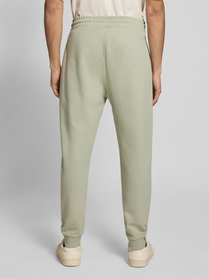Mężczyzna nosi Relaxed Fit Sweatpants aus reiner Baumwolle Modell 'NAPIN' od Hugo Blue, jednokolorowy efekt, krój relaxed fit, naszywka z logo, tunel, elastyczny ściągacz w pasie, prążkowane zakończenia nogawek, wpuszczane kieszenie boczne, wykończenie: dzianina dresowa, materiał: czysta bawełna, widok całej sylwetki od tyłu.