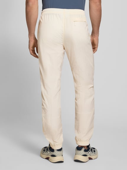 Männermodel trägt Straight Fit Stoffhose mit Logo-Stitching Modell 'Nayla' von SERGIO TACCHINI in Beige, elastischer Bund mit Tunnelzug, elastische Beinabschlüsse, Innenbeinlänge bei Größe M 77 cm, Ganzkörperansicht Rückansicht.