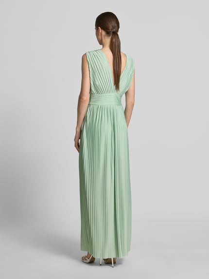Frauenmodel trägt Abendkleid mit V-Ausschnitt Modell 'Linnea' von GUIDO MARIA KRETSCHMER WOMAN aus grünem Chiffon mit Plisseefalten, Maxikleid, Taillierter Schnitt, Rückseitiger V-Ausschnitt, seitlicher Nahtreißverschluss, Ganzkörperansicht Rückansicht.