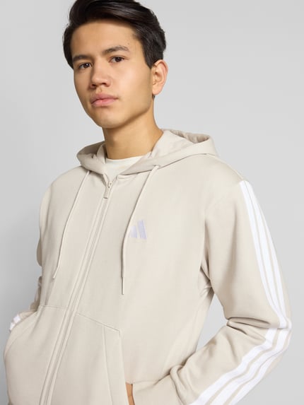 Männermodel trägt Regular Fit Sweatjacke mit Viskose-Anteil von adidas Sportswear, beige, Logo-Stitching, Nahaufnahme Oberkörper, Baumwoll-Mix