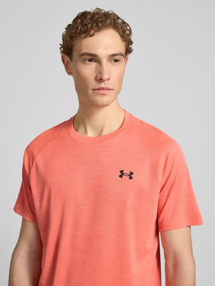 Mannenmodel draagt t-shirt met labelprint model 'Tech' van Under Armour in koraal, recht model, ronde hals, ruglengte maat M 75 cm, Nahaufnahme Oberkörper.