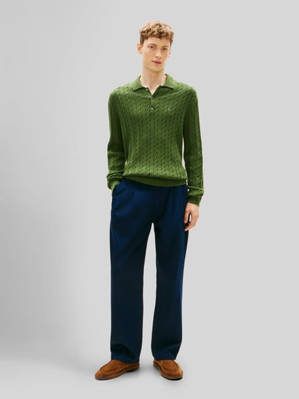 Männermodel trägt Regular Fit Strickpullover aus reiner Baumwolle von Tommy Hilfiger in Grün mit Zopfmuster, unifarben, Ganzkörperansicht von vorne.