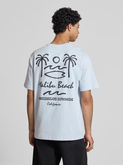 Männermodel trägt Relaxed Fit T-Shirt aus reiner Baumwolle Modell 'MILO' von Only & Sons, unifarben, Schriftzug-Print, kurzarm, Ganzkörperansicht Rückansicht