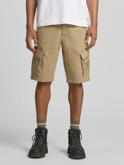 Männermodel trägt Bermudas mit Pattentaschen und Label-Stitchings von PME Legend in Beige, Straight Fit, Motiv-Stitchings, Eingrifftaschen, Knopf-Reißverschluss, Ganzkörperansicht von vorne.