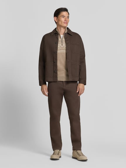 Männermodel trägt Wollpullover mit Label-Patch Modell 'Liaset' von Dale of Norway in Beige, kombiniert mit brauer Jacke und Hose, Gerade Schnitt, Troyer-Kragen, Reine Wolle, Ganzkörperansicht von vorne.