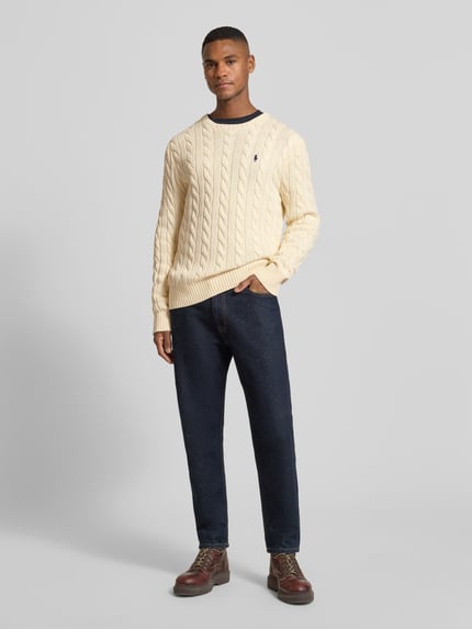 Männermodel trägt Strickpullover mit Label-Stitching von Polo Ralph Lauren, Regular-Fit, Reine Baumwolle, Rundhalsausschnitt, Gerippte-Abschlüsse, Dunkelblaue Hose, helle und strukturierte Pullover-Optik, Ganzkörperansicht von vorne.